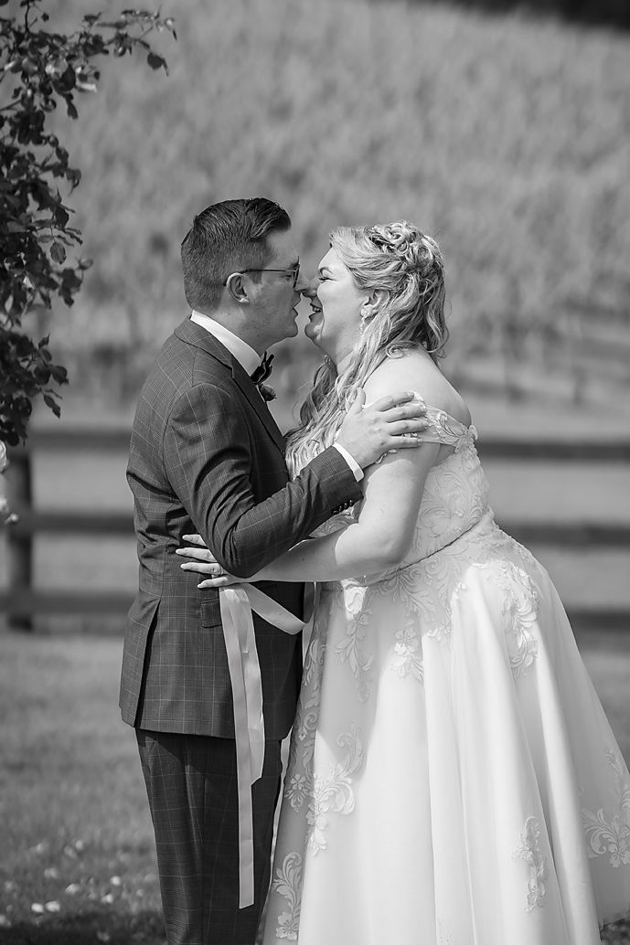 A tender black and white moment between newlyweds in formal wedding attire, captured in a garden setting.