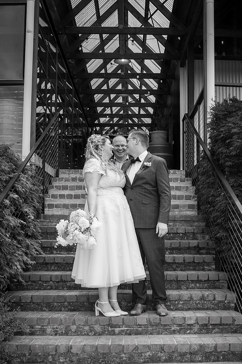 Black and white wedding photograph on brick steps with an architectural roof structure above.