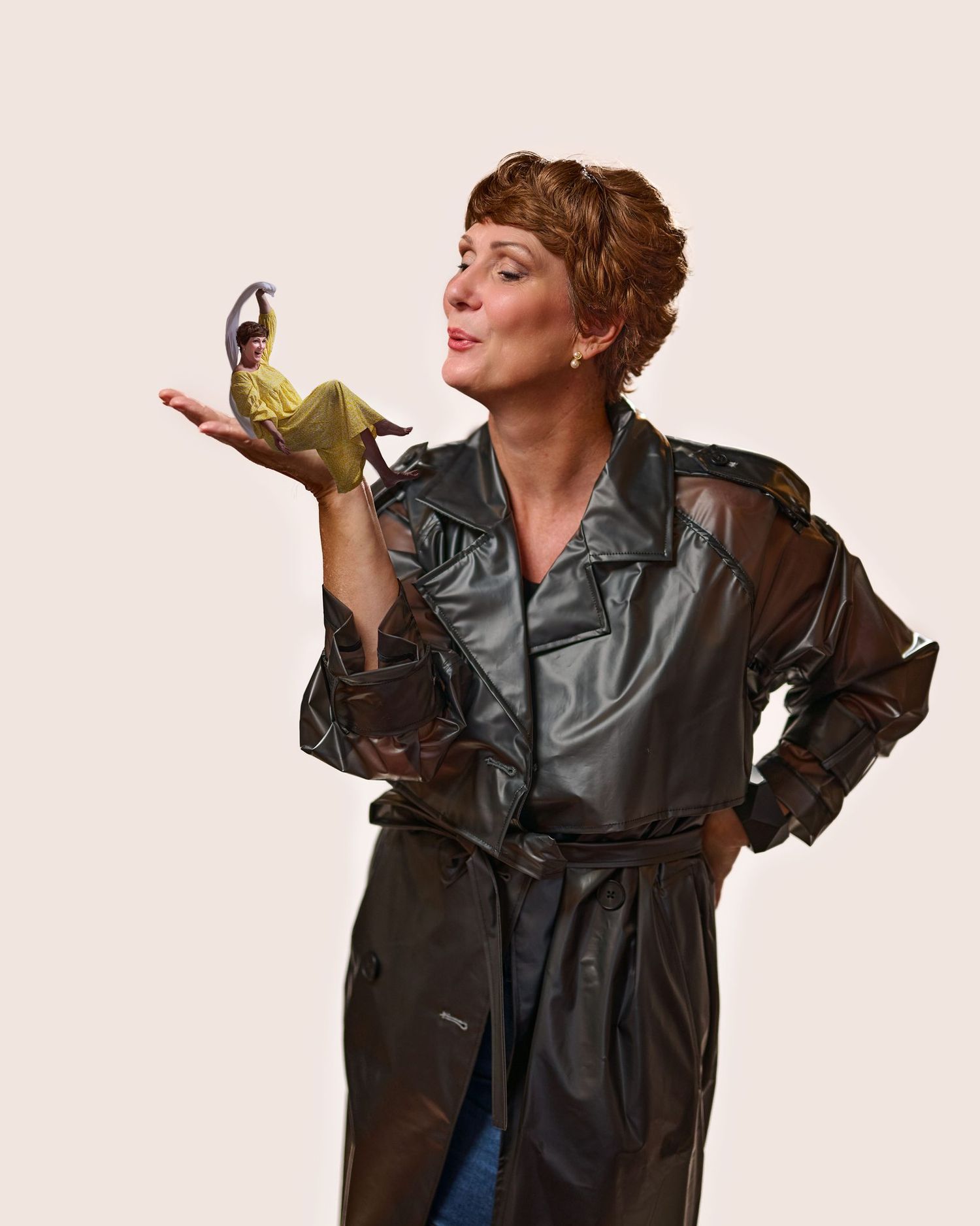 Someone wearing a silver trench coat holds up a small object while posing dramatically against a light background.