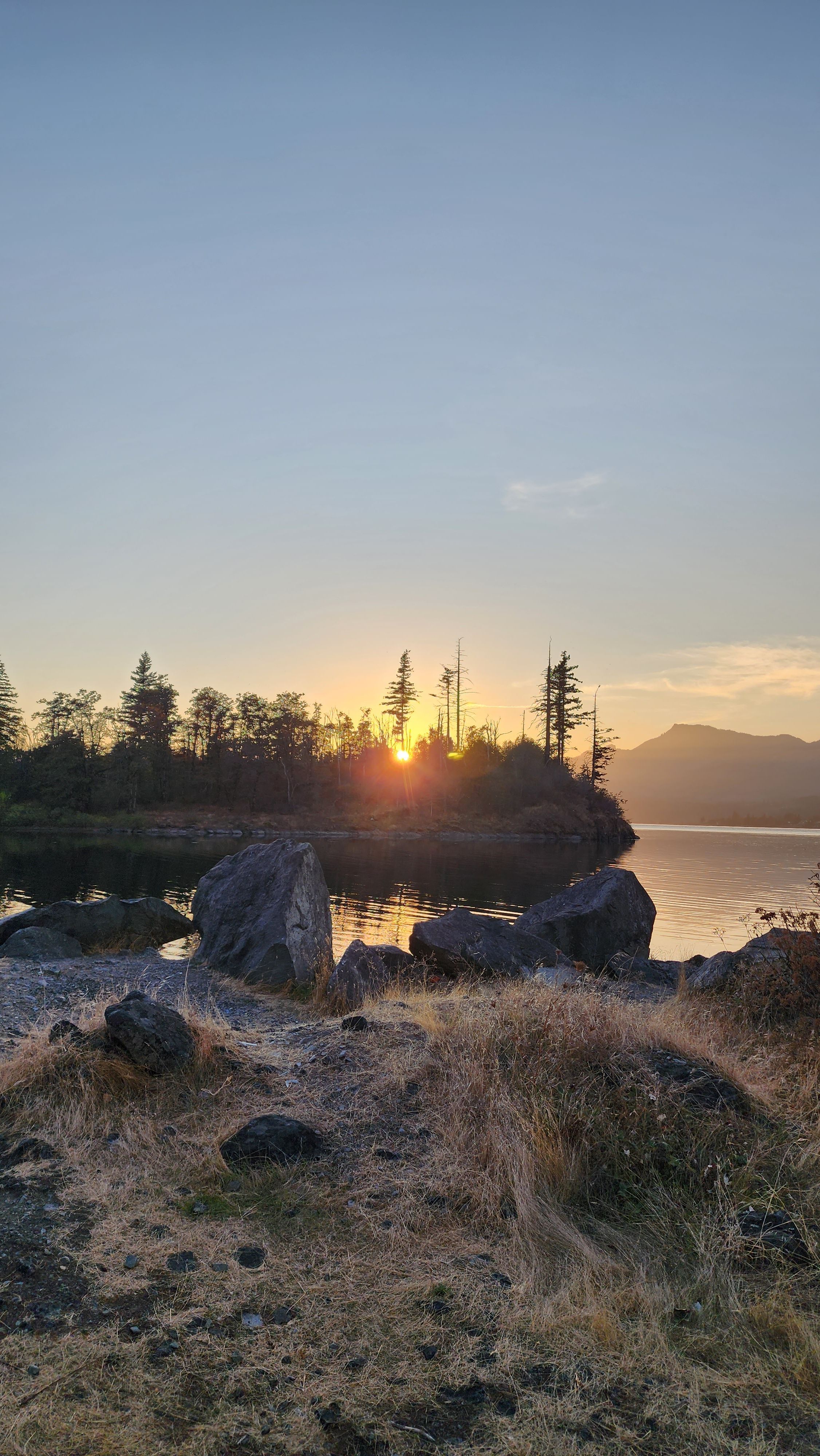 Dramatic Columbia River sunset with rocky cliffs and silhouetted trees.