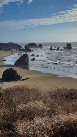 Rocky shoreline with waves breaking under a blue sky.