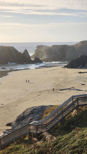 Oregon Coast beach with large sea stacks and a few people walking along the sand.