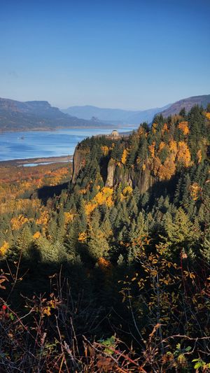 Sunlit cliffs with Vista House with forested hills and deep shadows in the valley.