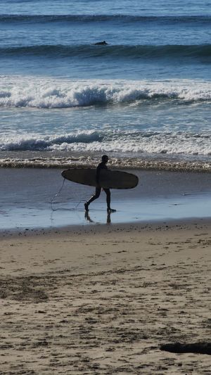Surfer walking with surfboard along the shoreline at the Oregon Coast.