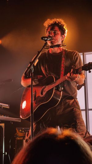 Musician performing live on stage under warm spotlight.
