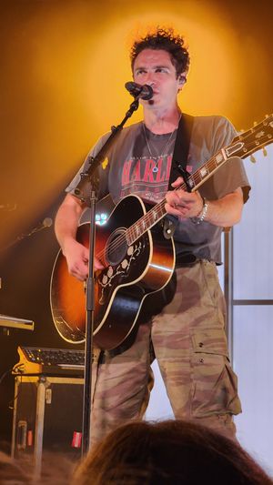 Marc Scibilia live performing on stage with guitar under warm stage lights.