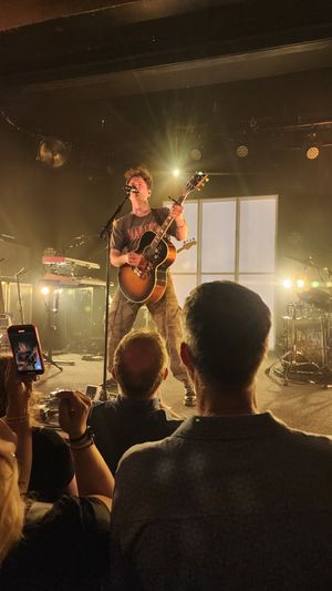 Music performance with a guitarist singing on stage in front of an audience.