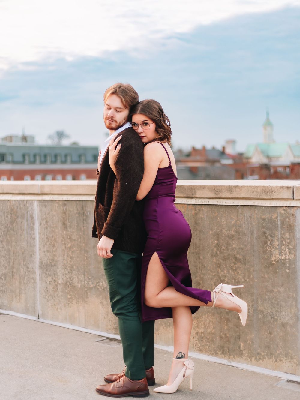 A couple shares a romantic moment on a concrete rooftop against an urban backdrop.