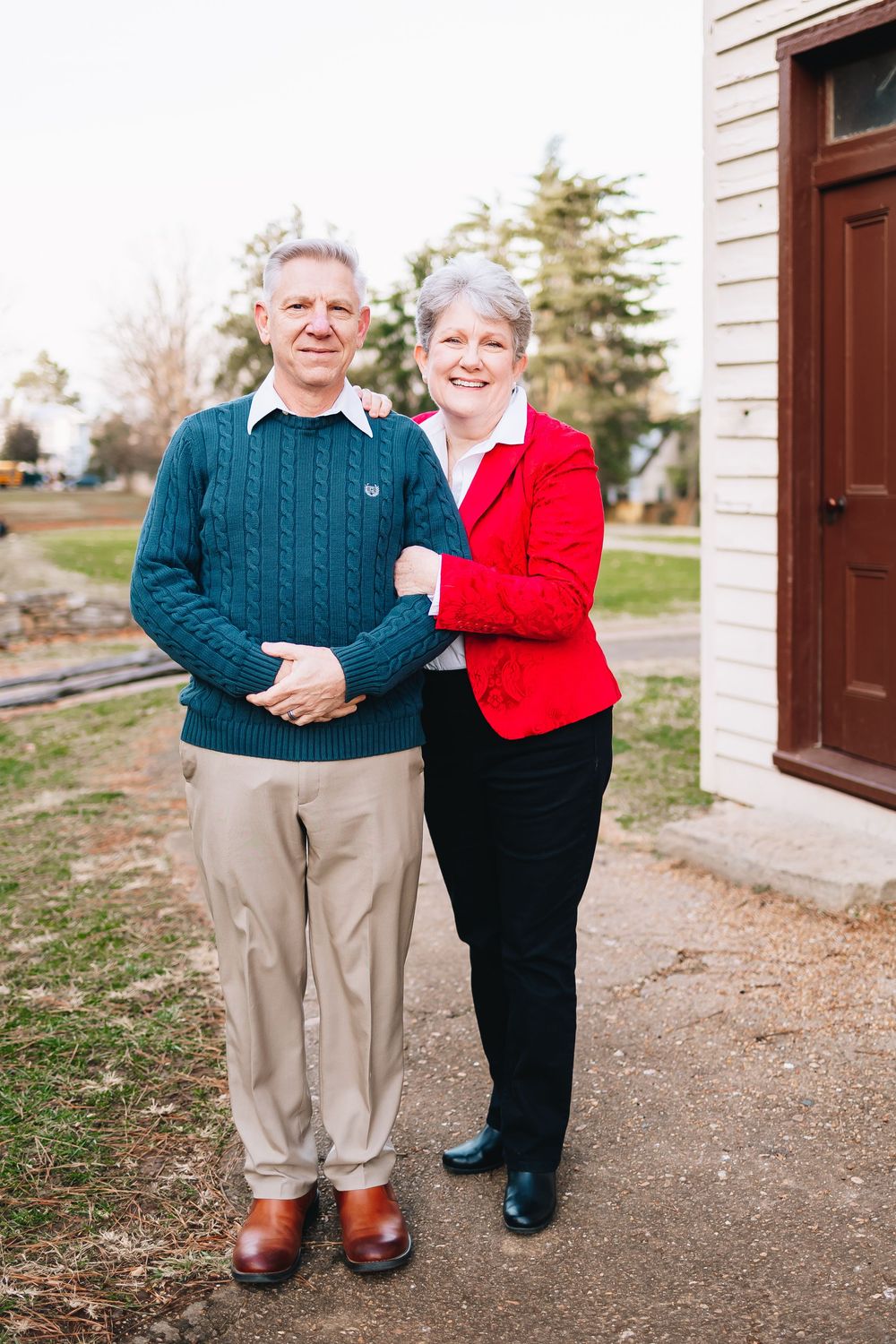 A mature couple poses together outside a building in casual winter attire.