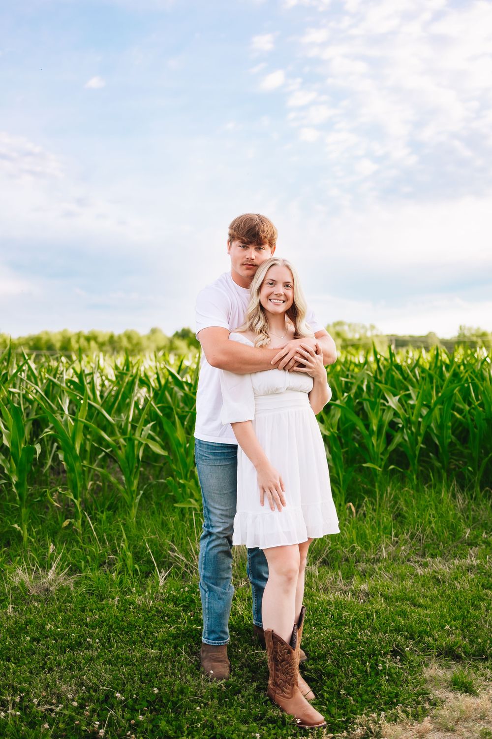 A couple embraces tenderly near a cornfield on a sunny afternoon.