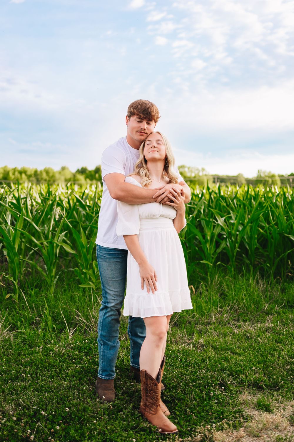 A couple shares an intimate moment by a cornfield against a blue summer sky.