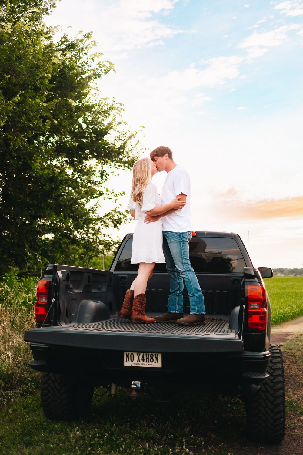 A couple shares a romantic moment in the bed of a black pickup truck at sunset.