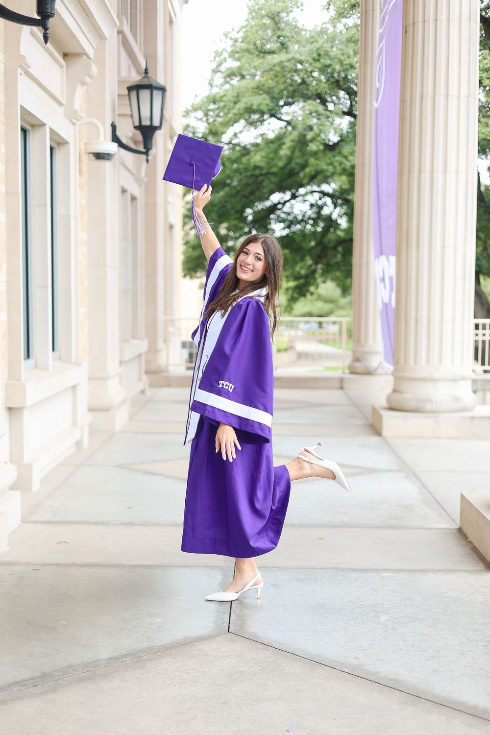 Purple graduation cap and gown twirl against classical white columns.