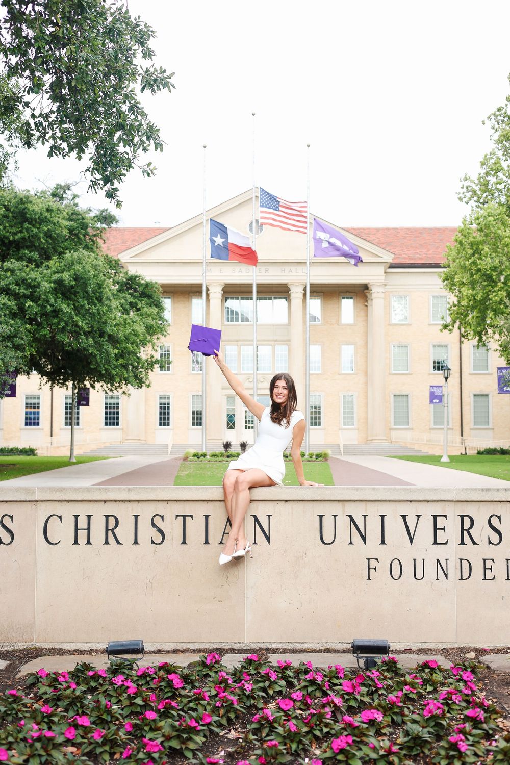 University entrance with flags and flower beds serves as backdrop for graduation celebration.