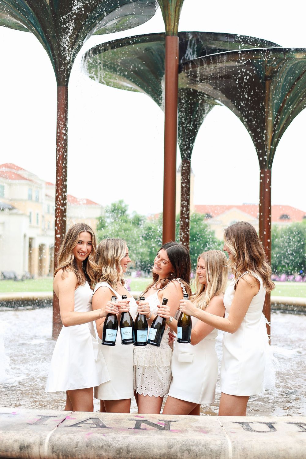 Champagne sprays during a celebratory photo session under classical columns.