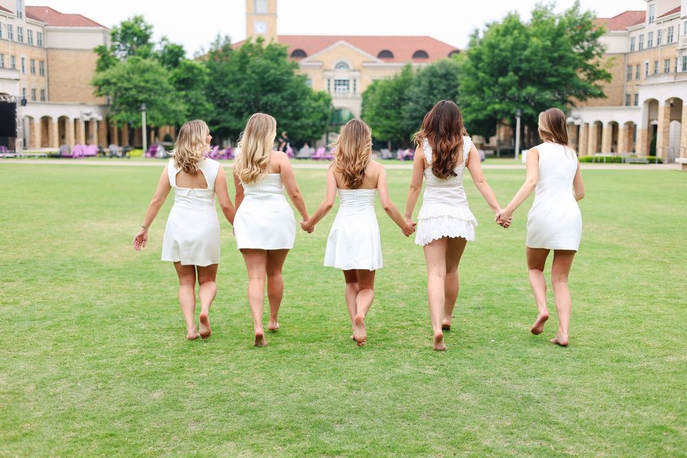 Friends walk hand in hand across a grassy field in matching white outfits.
