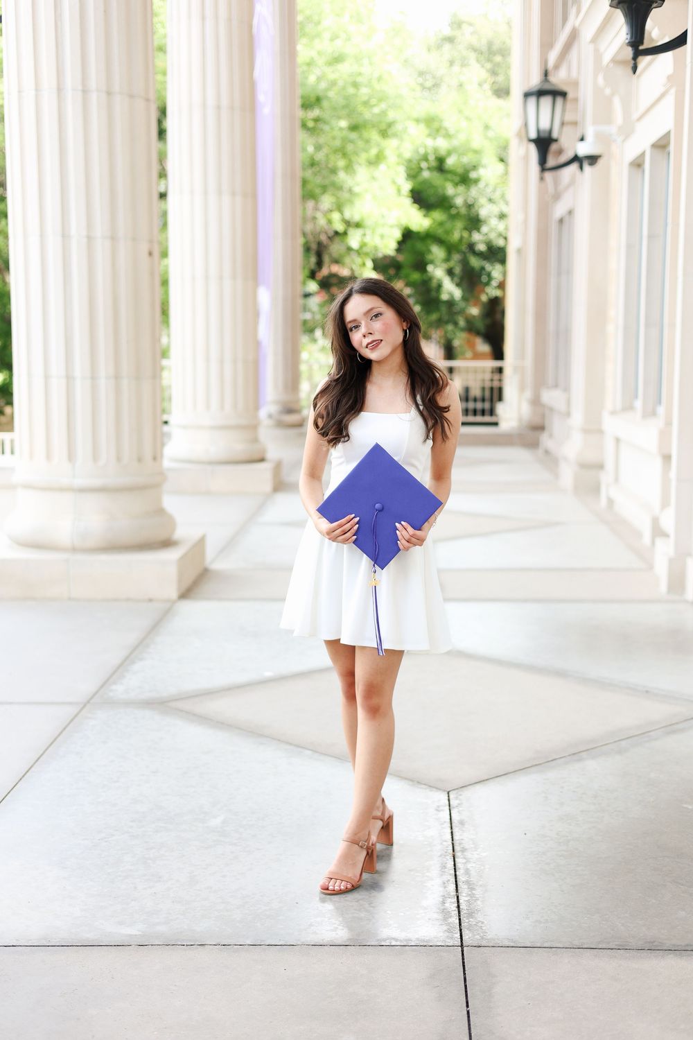 Sunlit colonnade with white columns frames a graduation photoshoot scene.