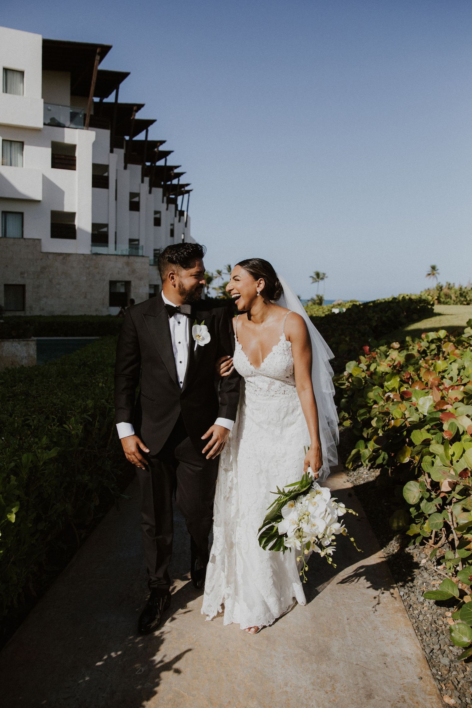 Newlyweds share intimate moment outside modern resort building with ocean view.