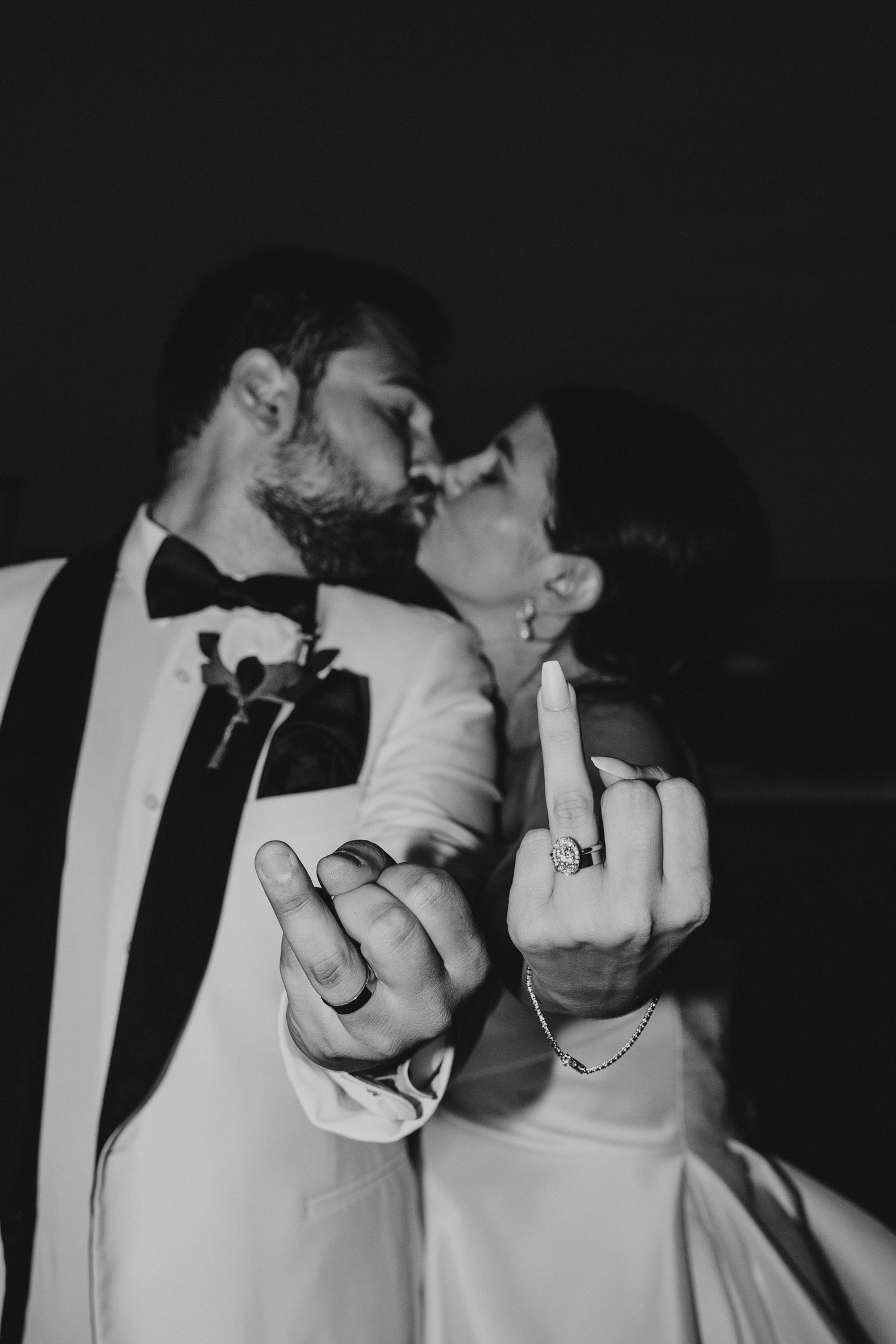 A playful black and white portrait of newlyweds showing off their rings in a humorous pose.
