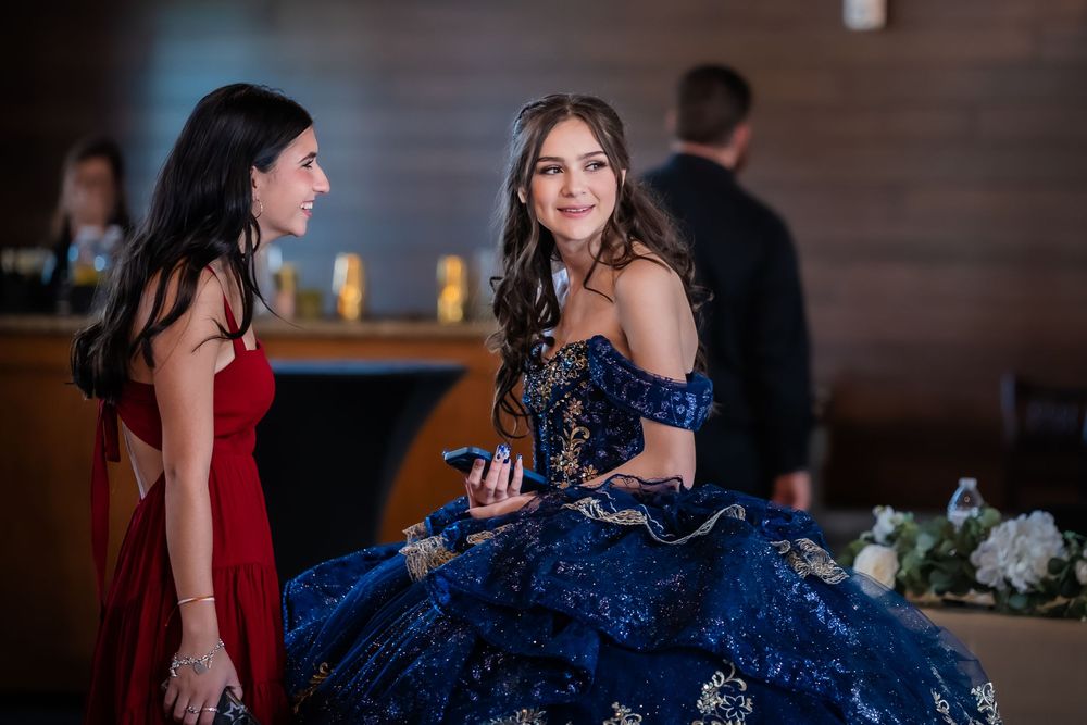 Two women near a bar area, one wearing a stunning navy blue formal gown with intricate embellishments.
