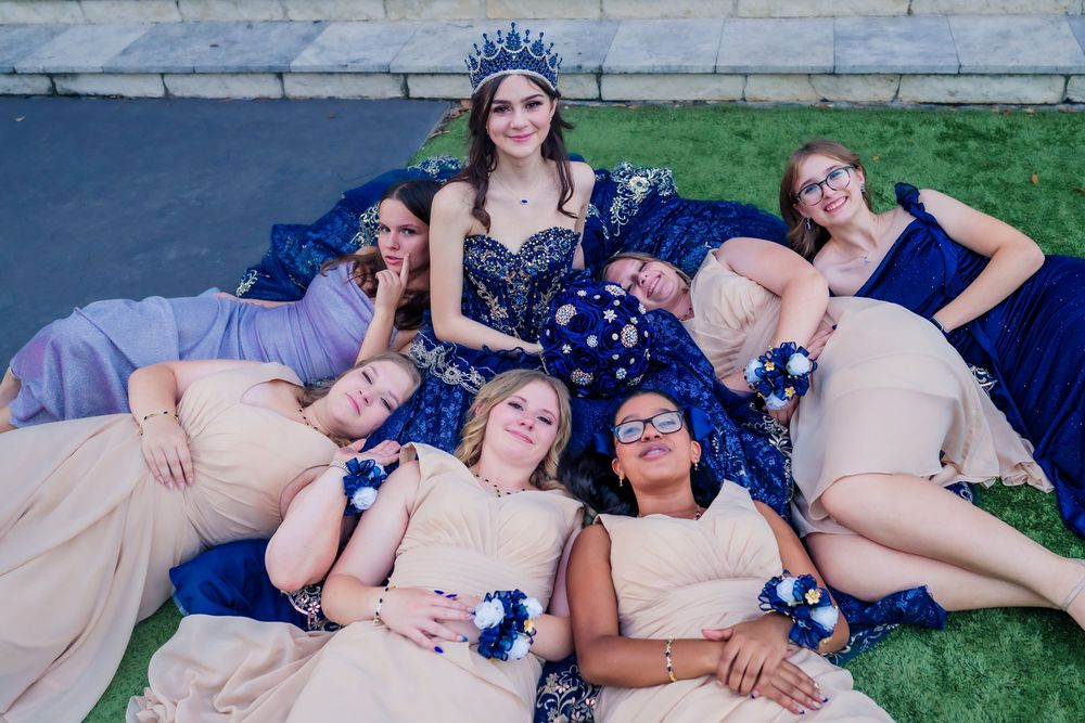 A group in coordinated navy and beige formal attire lies on grass in a playful photo composition.