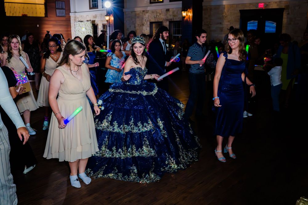 Guests dancing at a festive event with a formal dress code featuring an ornate navy blue ballgown on the dance floor.