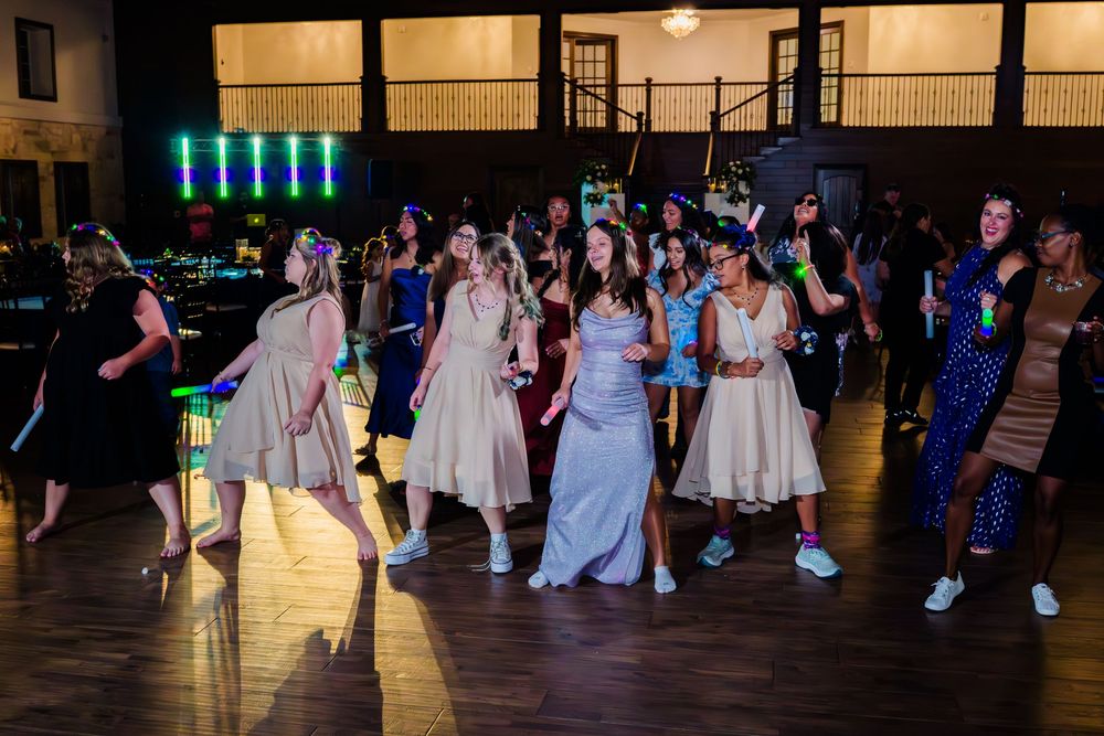 Wedding reception guests dance on a dimly lit ballroom floor under blue lighting during an evening celebration.