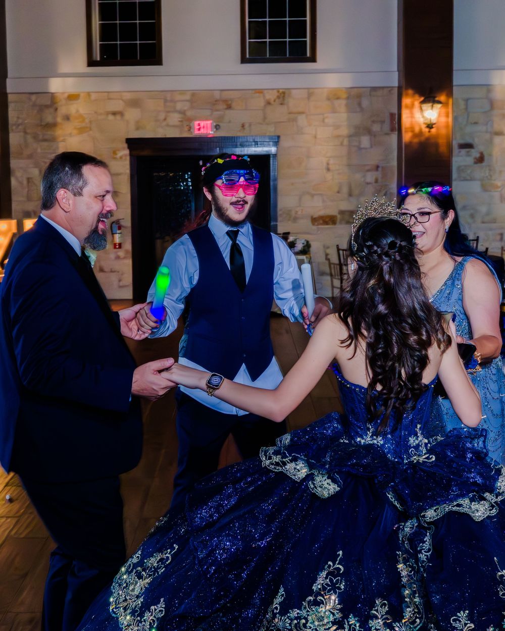 Guests in formal attire dancing and mingling at an elegant wedding reception with stone walls and dim lighting.