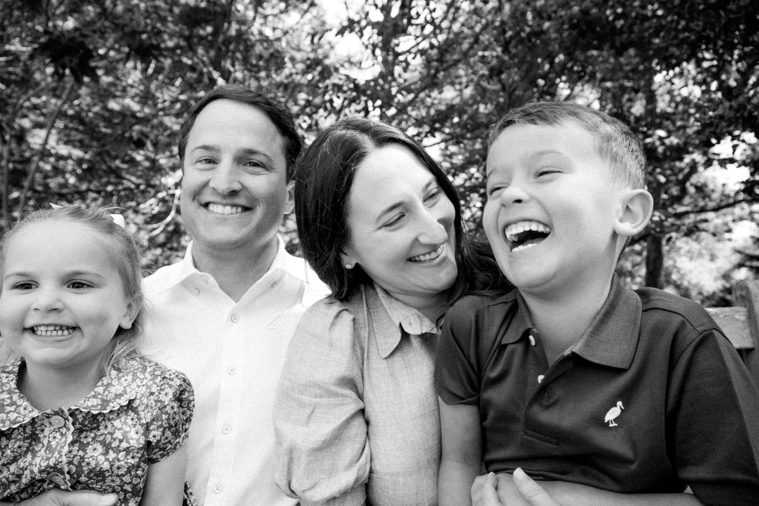 A joyful black and white family portrait shows genuine laughter and smiles in an outdoor natural setting.