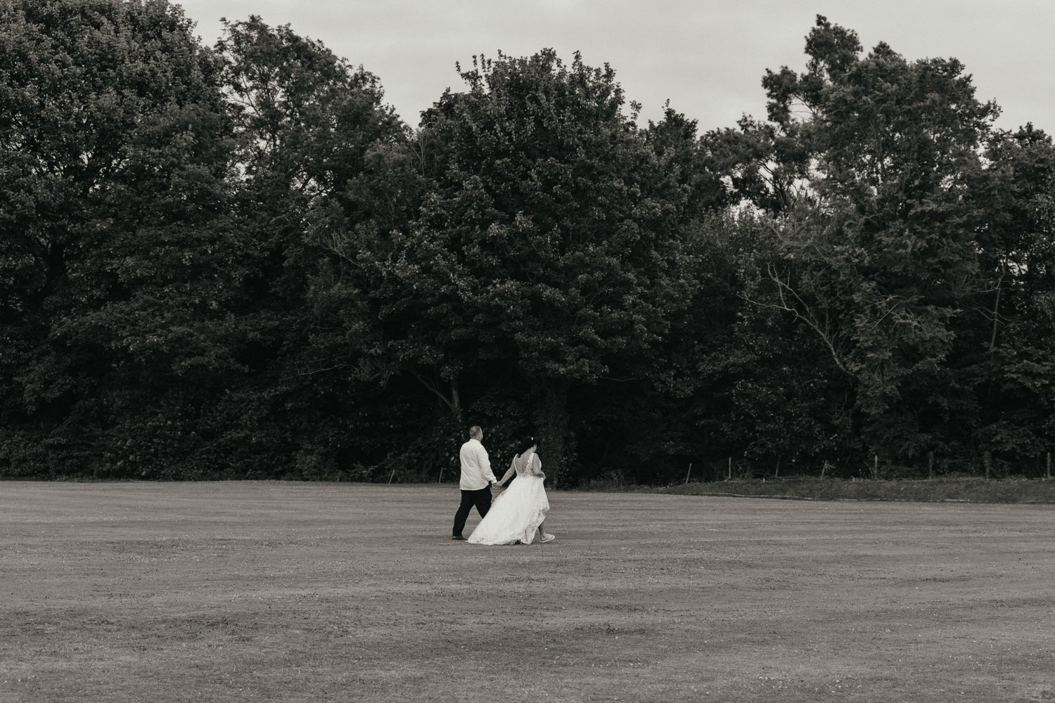 Black and white wedding photos arranged in a panoramic sequence showing couple moving across grassy field at sunset.