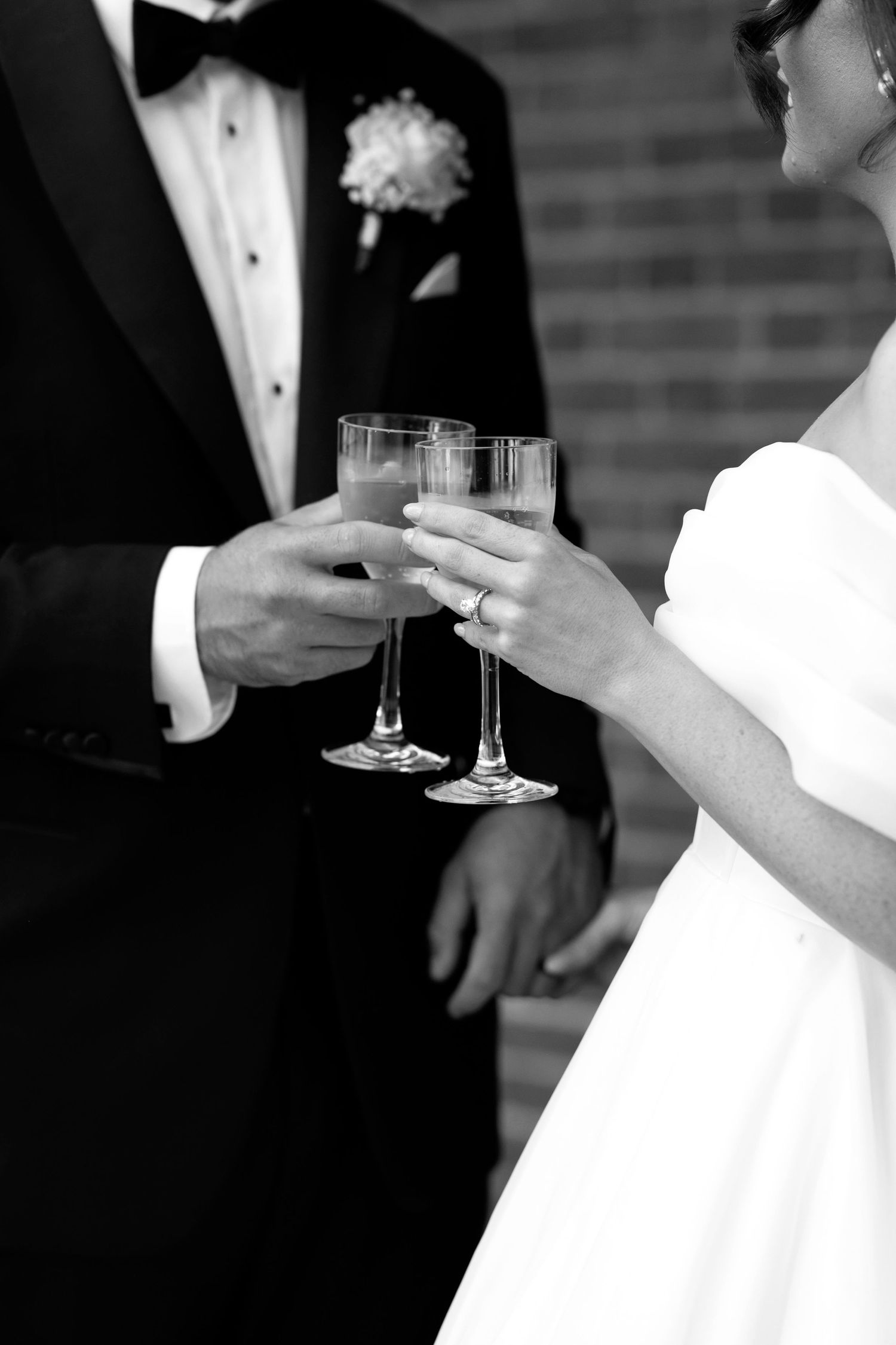 Black and white photo of elegant hands holding champagne glasses during a formal event.
