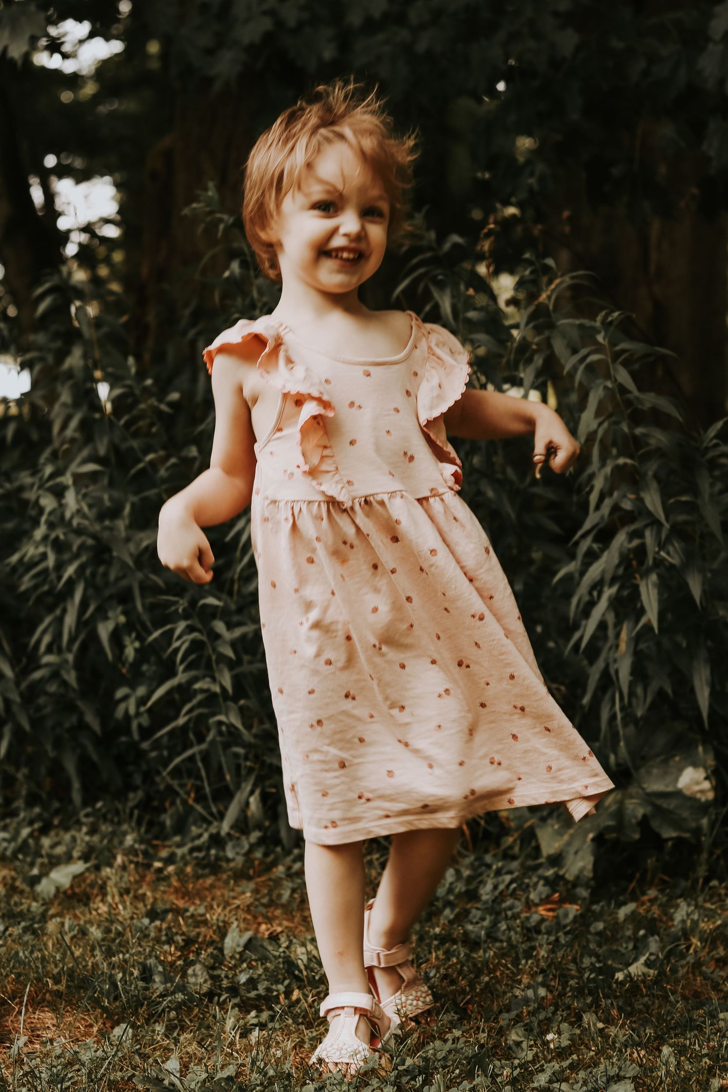 A toddler wearing a light pink polka dot dress plays in a garden setting during golden hour.