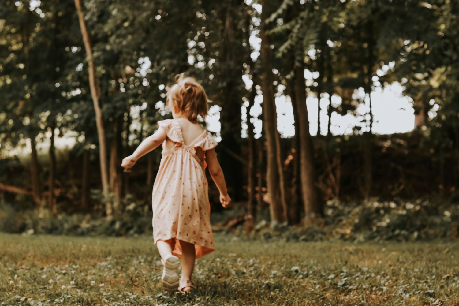 Candid shot of a toddler running through a sunlit garden wearing a peach-colored dress.
