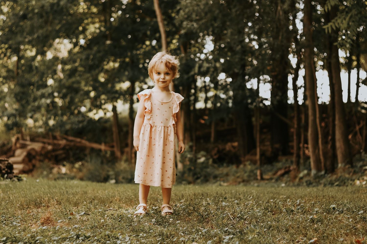 Toddler in a delicate dress enjoys playtime in a serene forest setting.