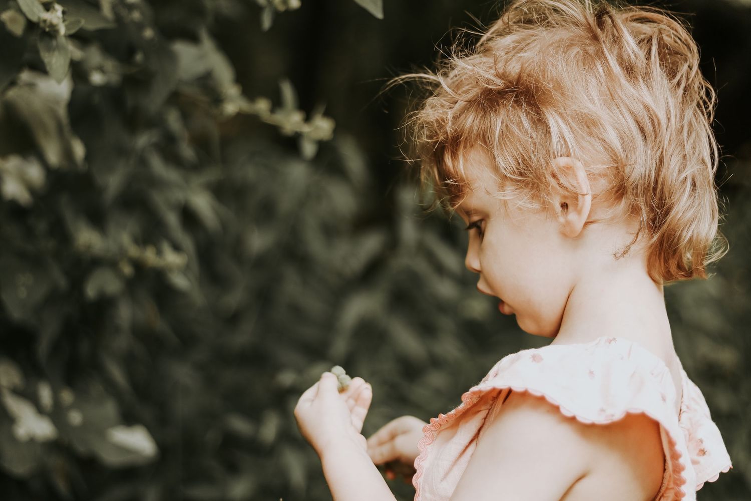 Child in vintage-style dress plays among trees during golden hour photography session.