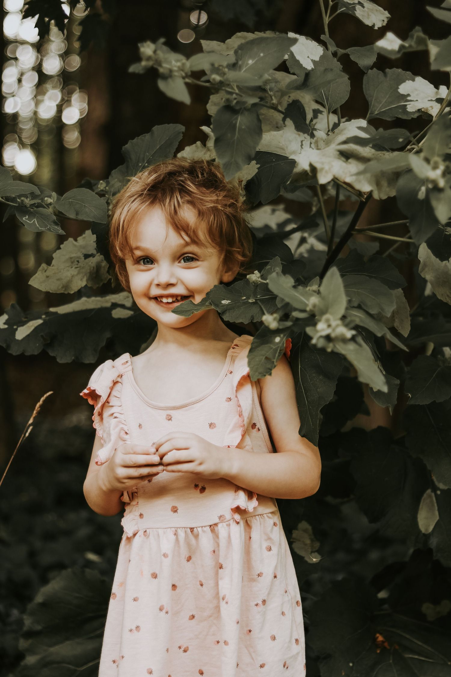 A sweet pink polka dot dress with ruffles is worn outdoors against a leafy green background.
