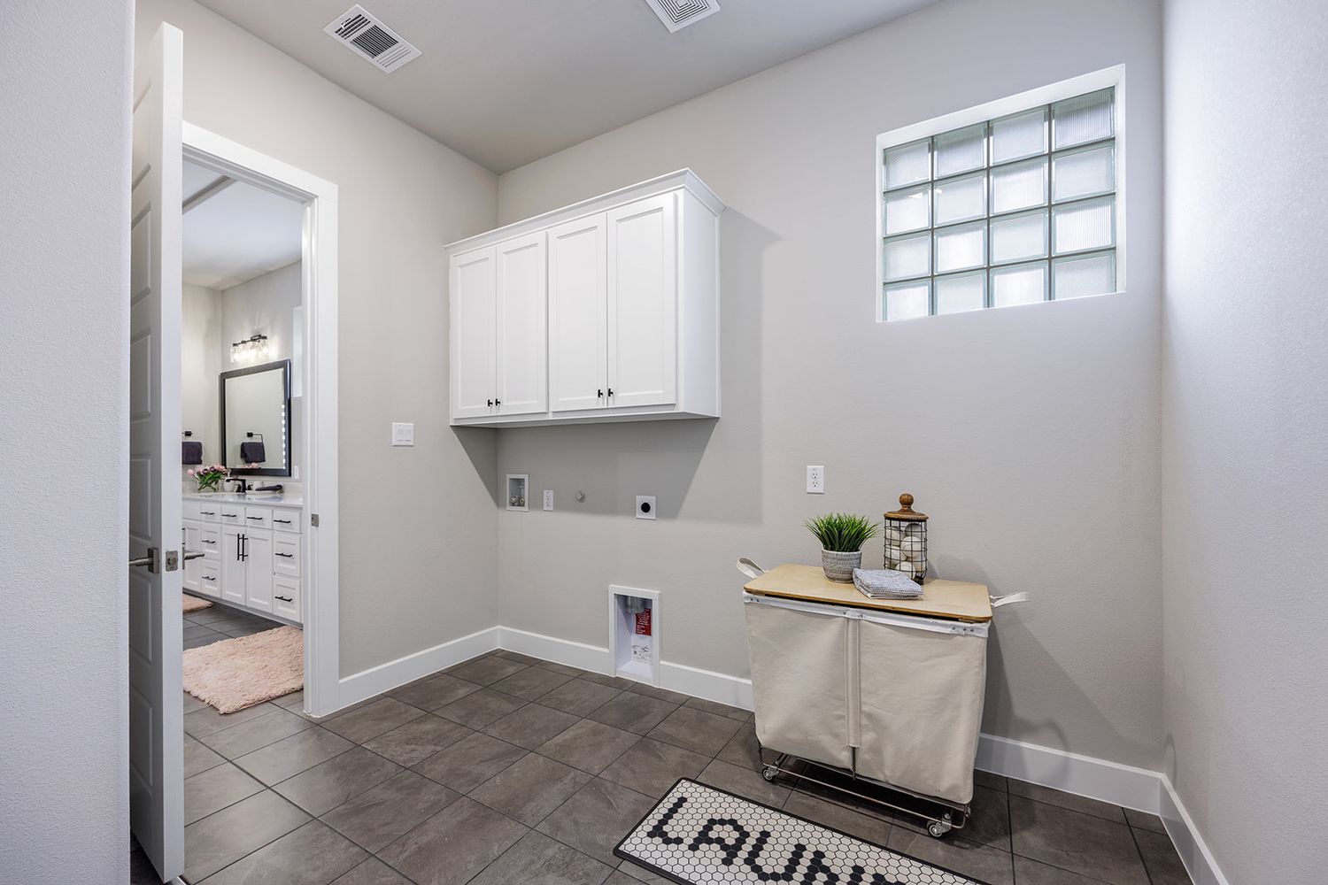 Modern laundry room with white cabinets, gray tile floors, a small window and a decorative 'Laundry' floor mat.