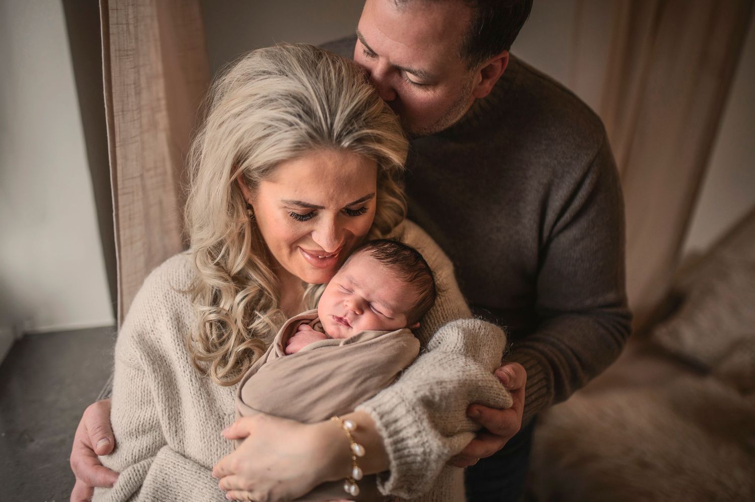 Parents snuggling with their newborn baby in cozy living room during intimate lifestyle photo session.