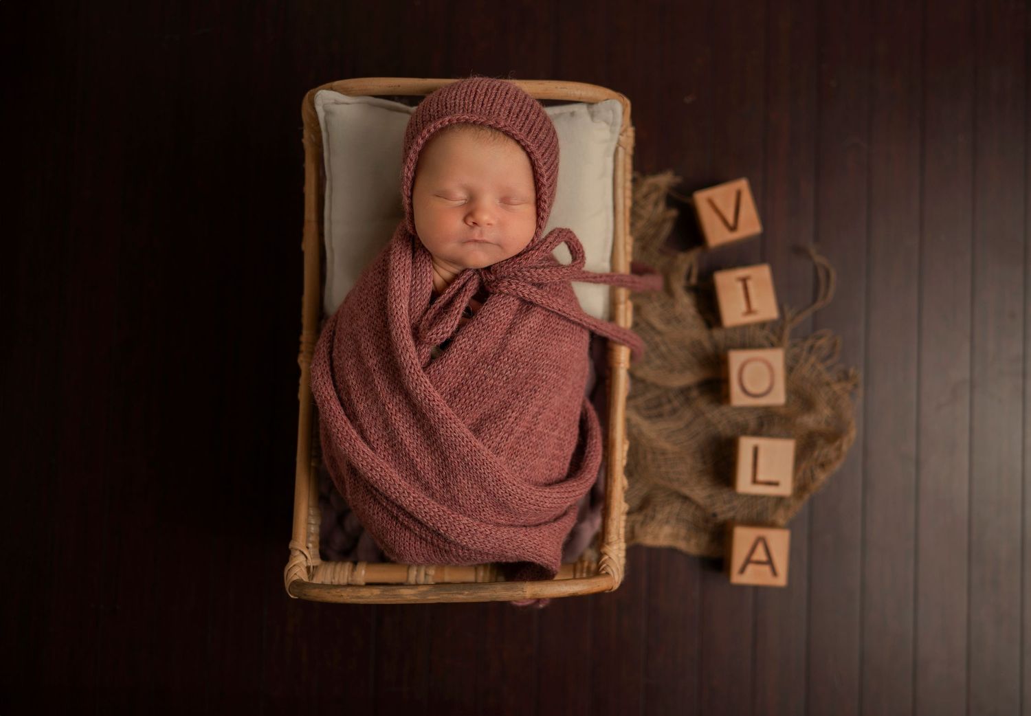 A row of newborn photography shots shows a baby in burgundy wraps positioned in woven baskets with wooden blocks.