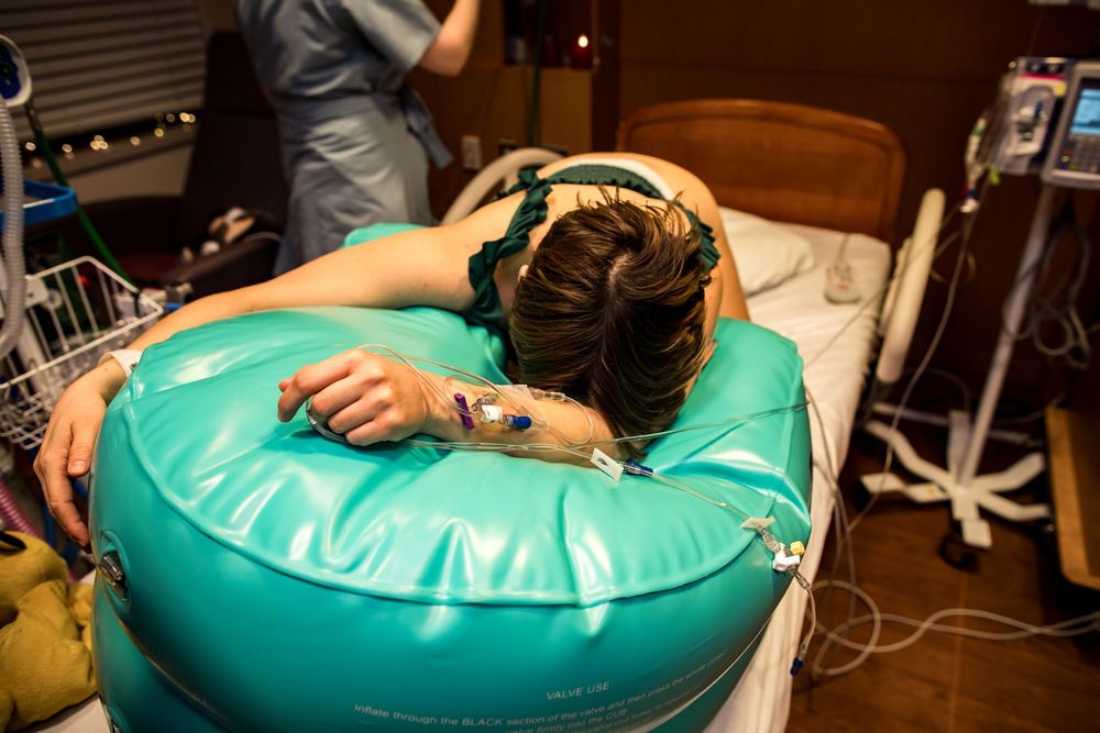 Patient resting on a teal-colored medical support cushion in hospital room.