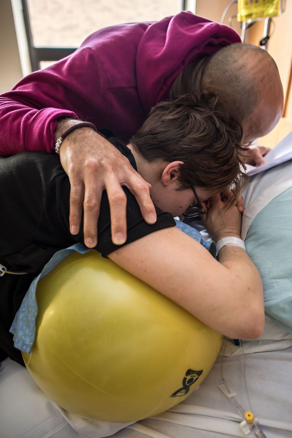 Patient receiving care while resting on yellow therapy ball in hospital bed.