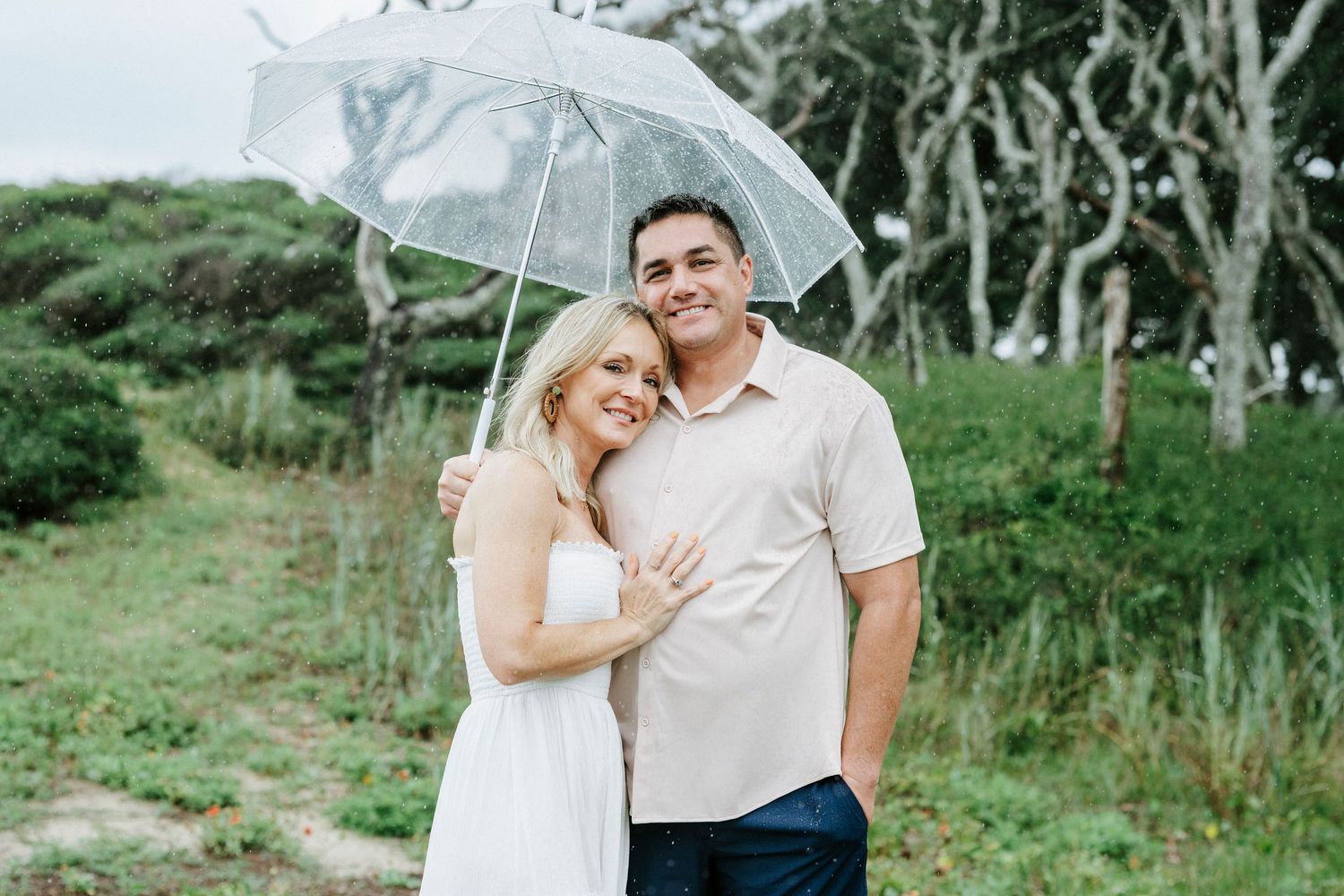 Couple embracing under clear umbrella against natural coastal landscape.