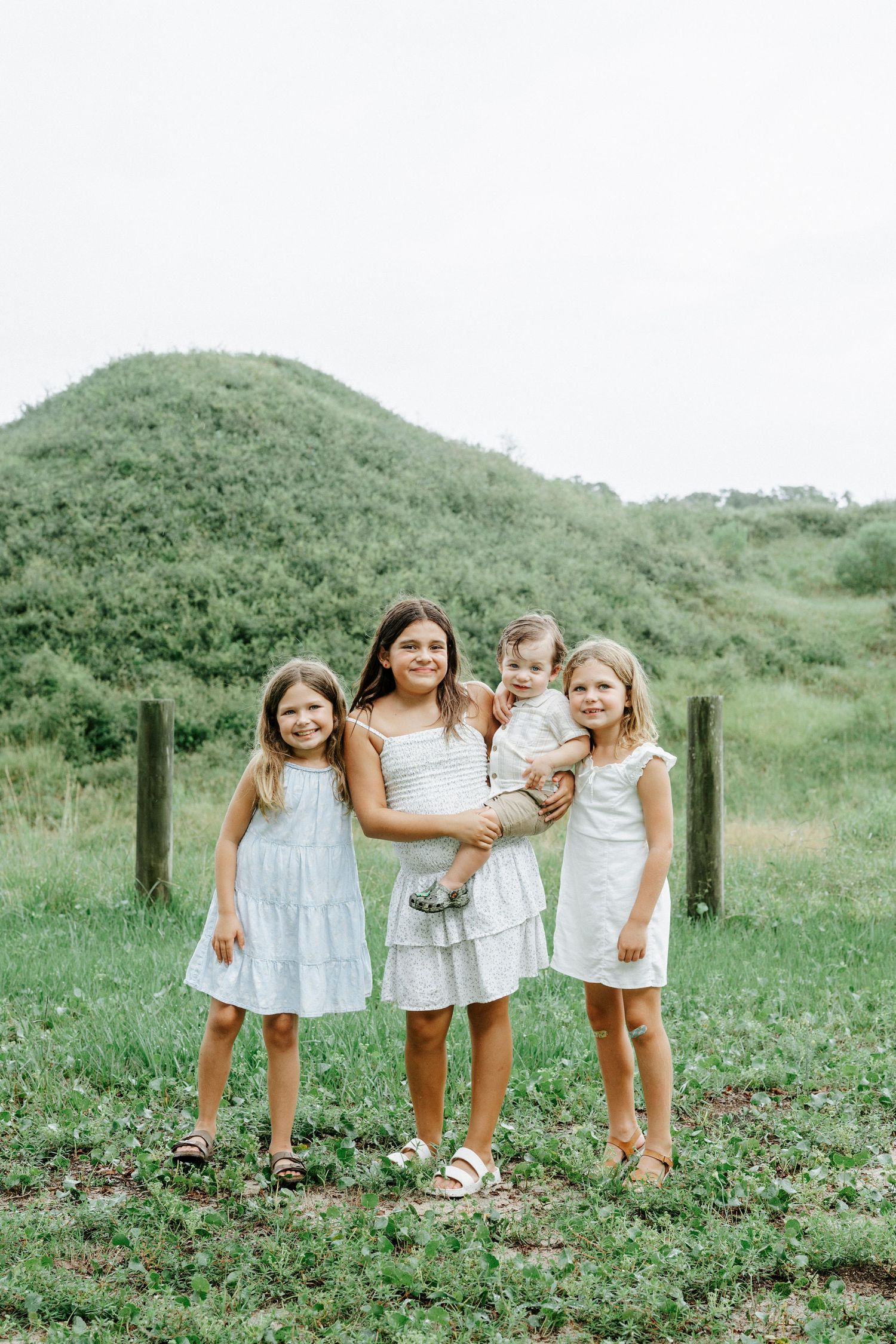 Children in white outfits posing together on grassy hillside.