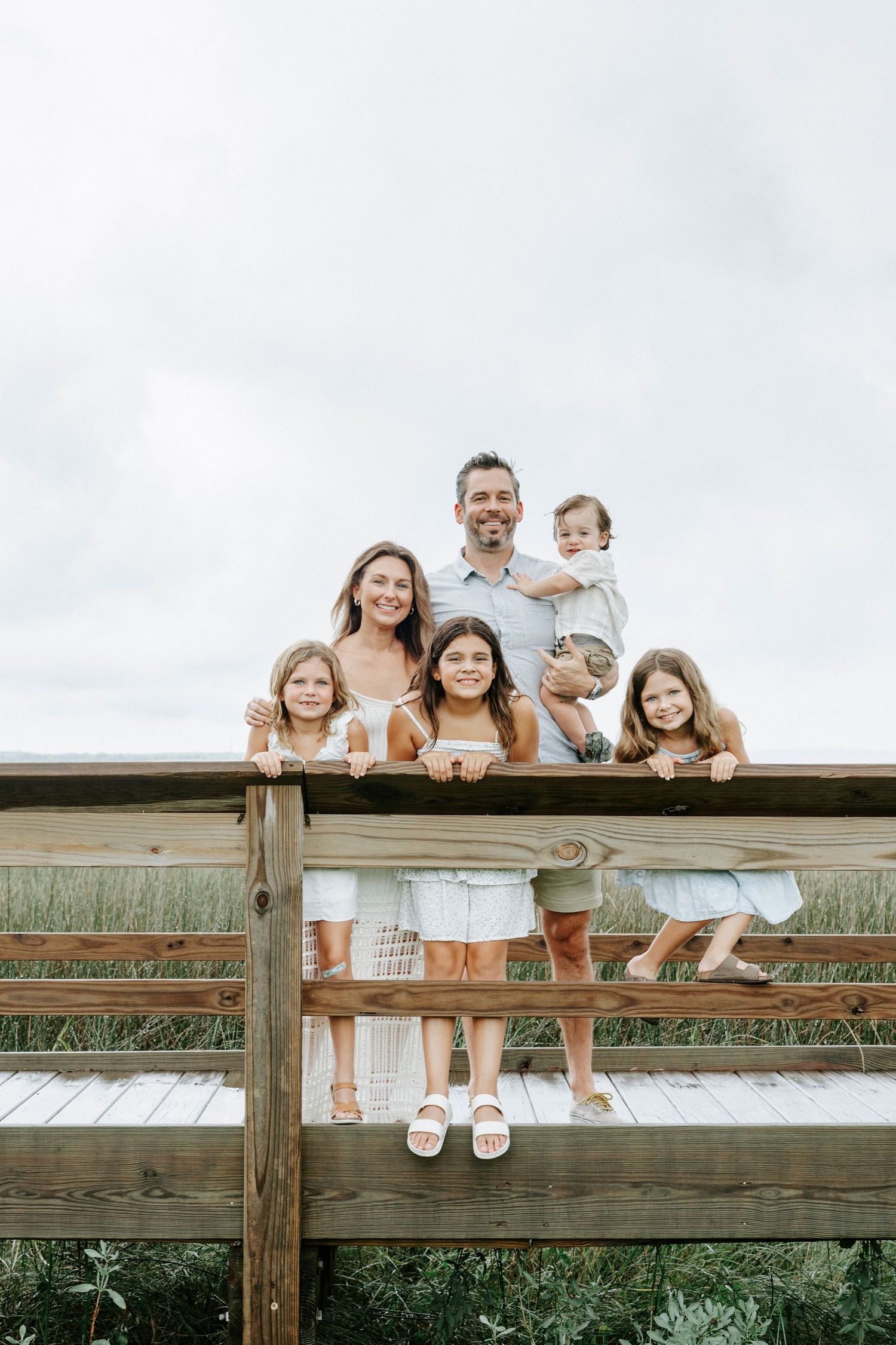 Family members sitting together on wooden fence with sky in background.