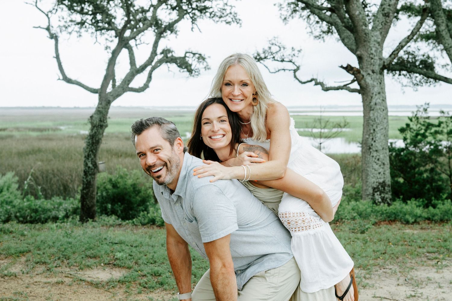 Group embraces and laughs together during outdoor photo session under sprawling oak tree.