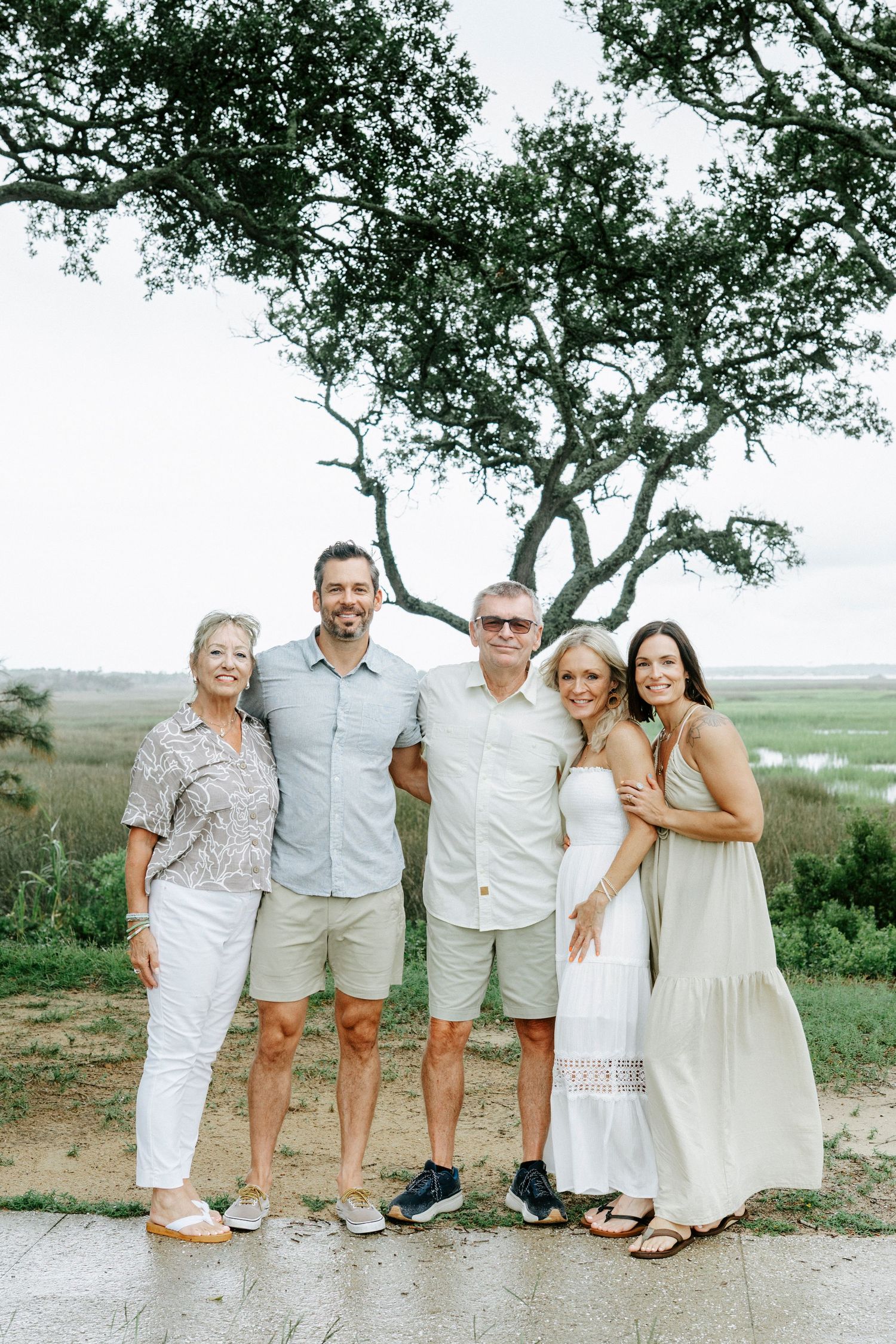 Family group wearing coordinated white and beige outfits poses together on coastal path.