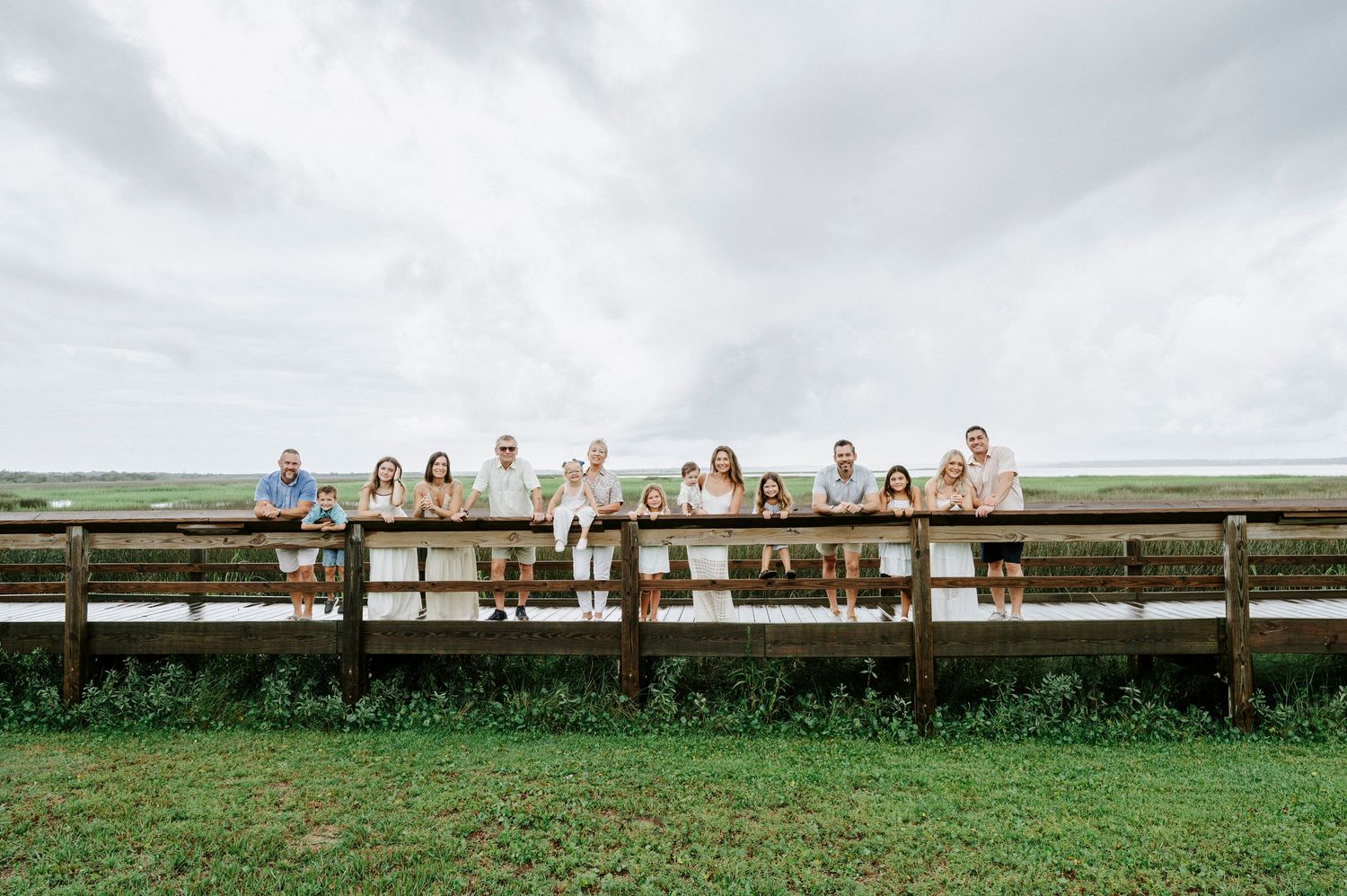 Extended family members sit spaced apart on long wooden boardwalk for panoramic photo.