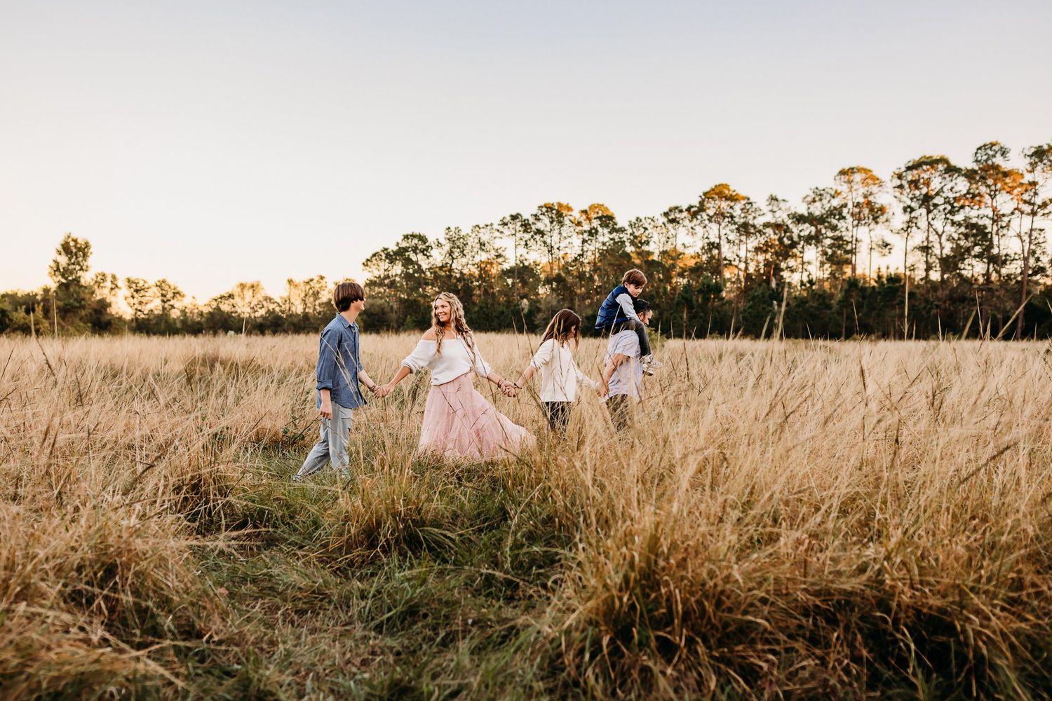 People stroll together through a golden field of tall grass during sunset creating a dreamy outdoor scene.