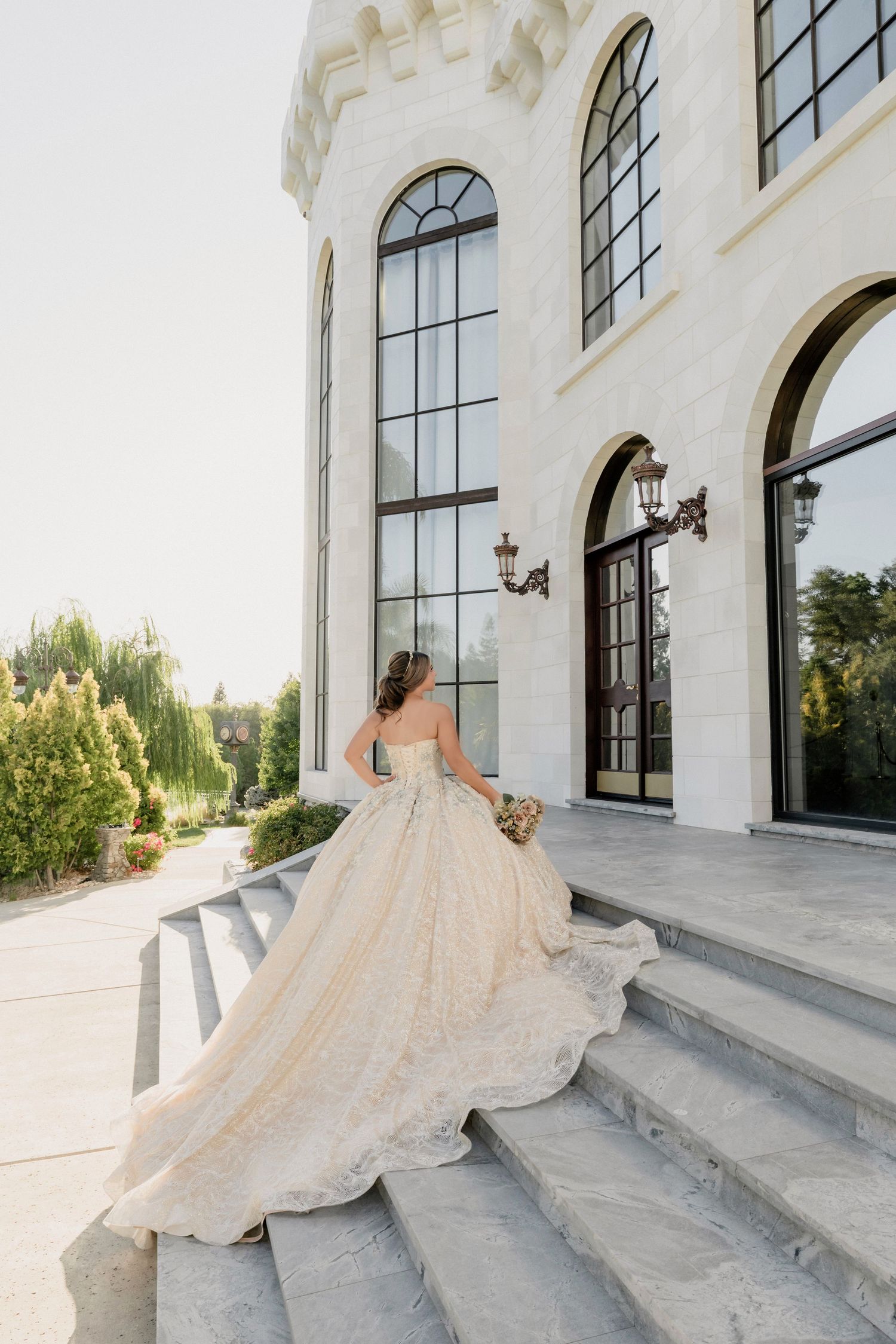 Flowing champagne-colored ballgown dress photographed on white stone steps of an elegant building.