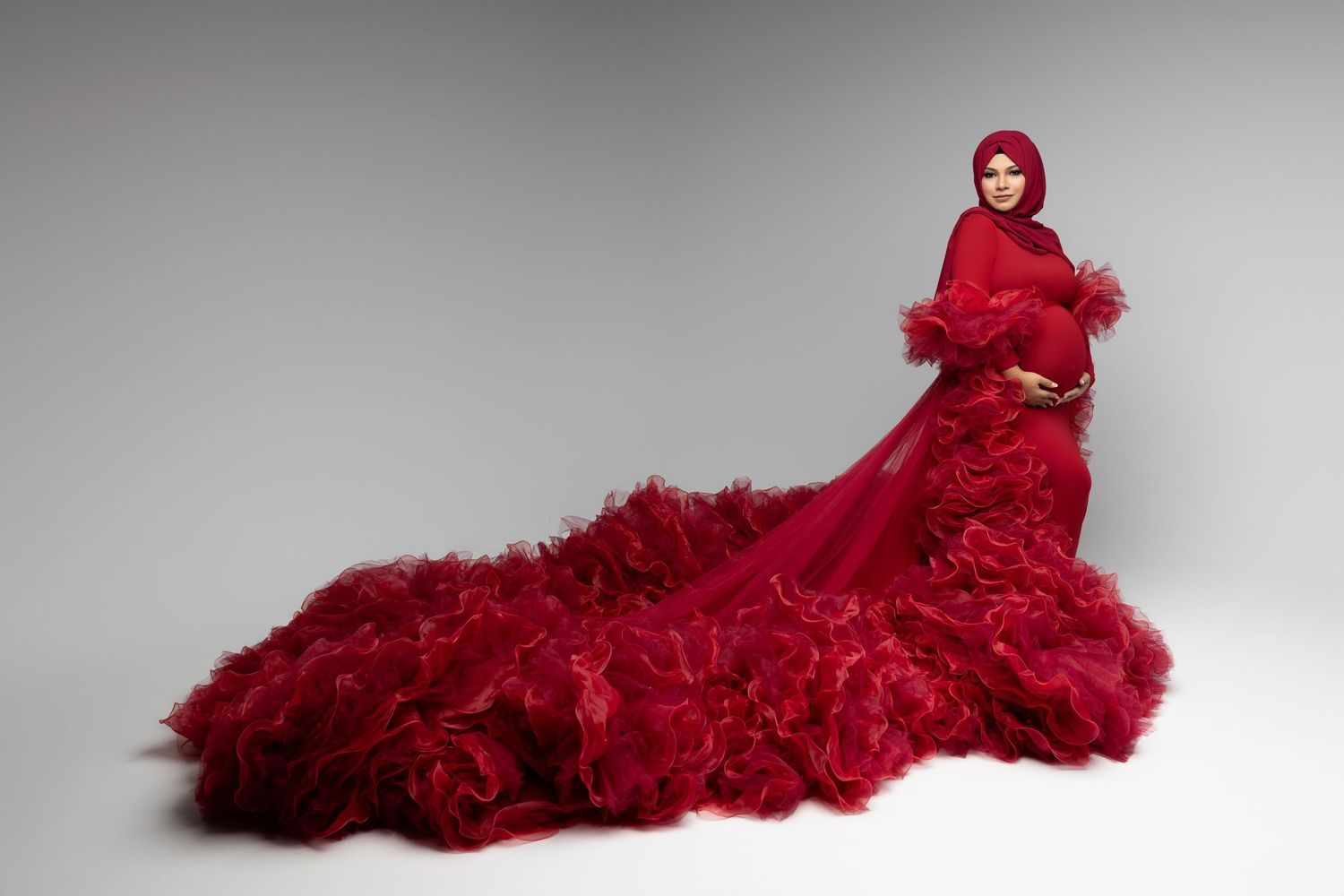 A dramatic red couture gown with ruffled train and matching hooded cape photographed against a white background.